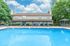 Inviting apartment pool area with comfortable lounge chairs, surrounded by lush greenery and a clear blue sky.