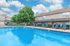 Inviting community pool area with cozy lounge chairs under a bright blue sky, surrounded by lush greenery and modern townhomes.