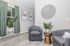 Cozy modern living area with stylish gray armchairs, lush green plants, and elegant decor, featuring a chic oversized wall clock.
