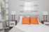 Bright and cozy bedroom with modern bedside tables, orange accent pillows, and soft natural light filtering through striped curtains.