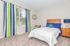 Bright and cozy bedroom with a comfortable wooden bed, colorful striped curtains, and a charming blue lamp.