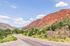Scenic road with lush greenery and vibrant red rock mountains under a clear blue sky.