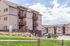 Inviting apartment complex showcasing multiple balconies, surrounded by lush greenery and clear skies, offering a welcoming community atmosphere.