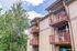 Charming apartment exterior with private balconies, surrounded by lush greenery and a bright blue sky.
