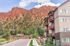 Modern apartment building with charming balconies set against stunning red rock cliffs and lush greenery.