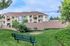 Charming apartment complex with inviting balconies, surrounded by lush green lawns and a peaceful park bench view.
