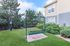Charming outdoor area with a green lawn, inviting swing, and lush landscaping beside a modern apartment building.