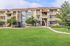 Charming three-story apartment building with spacious balconies, surrounded by lush greenery and a well-maintained lawn, perfect for comfortable and serene living.