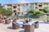 Inviting apartment complex showcasing a spacious outdoor lounge area with modern wicker seating and vibrant blue cushions, complemented by umbrella-covered tables and lush greenery.