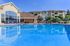 Luxurious apartment complex featuring a pristine swimming pool, inviting lounge chairs, and beautifully landscaped gardens under a clear blue sky.