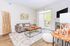 Modern and bright living room with a cozy beige sofa, stylish wooden coffee table, and elegant decor. Features a large window with sheer curtains leading to a balcony, and a chic floor lamp for ambient lighting.