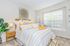 Bright and inviting bedroom with stylish decor, featuring a cozy bed with yellow accents, modern furnishings, and a large window providing natural light.