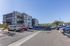 Modern apartment complex with spacious parking area, surrounded by lush greenery and a clear blue sky backdrop.