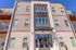 Modern apartment building exterior with large windows and balconies, set against a clear blue sky.