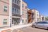Modern apartment complex with sleek architecture, spacious balconies, and ample parking in the foreground under a clear blue sky.