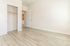 Bright and airy empty room with sleek hardwood flooring and an open closet, leading to a contemporary kitchen area.