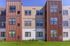 Modern apartment exterior with distinctive geometric design, featuring rich earth-toned panels and large windows, surrounded by lush green landscaping.