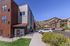Modern apartment complex with mountain views and ample parking, set against a clear blue sky.