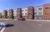 Modern apartment complex with three stories, featuring bold architecture and spacious parking area under a clear blue sky.