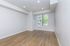 Bright and inviting apartment room with sleek wood flooring and large window offering a view of lush greenery.