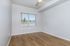 Bright and airy room with large window, gleaming hardwood floors, and modern ceiling fan.