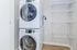 Modern apartment laundry room with stacked washer and dryer, featuring sleek white appliances and efficient shelving for storage.