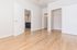 Bright bedroom with sleek hardwood flooring, open closet space, and doorway leading to modern kitchen area.