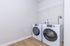 Modern laundry room with sleek white washer and dryer, featuring wood-look flooring and a convenient wire storage shelf.
