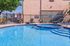 Inviting apartment pool area with sparkling blue water, relaxing lounge chairs, and lush greenery, perfect for summer days.