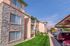 Charming apartment complex with stylish stone accents, lush green lawns, ample parking, and bright sunny skies.