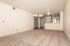 Spacious living area with cozy carpet flooring, elegant ceiling fan, and open-concept kitchen, perfect for modern living.