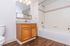 Bright and inviting bathroom featuring elegant wood cabinetry, a modern vanity mirror, and a sleek white tub with tiled surround.