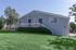 Charming single-story home with a light blue exterior, surrounded by lush green grass and mature trees.