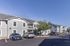 Charming apartment complex with modern grey siding, lush green landscaping, and convenient parking, basking under a clear blue sky.