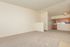 Bright living area with plush carpeting, open entryway, and cozy kitchen space, perfect for modern apartment living.