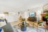 Inviting living room with a modern sofa, rustic armchair, stylish coffee table, and a cozy fireplace. Bright and airy space featuring a flat-screen TV and open layout to the dining area.