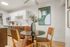 Modern dining area with a sleek round table, stylish woven chairs, and vibrant artwork, adjacent to a contemporary kitchen with chic cabinetry.