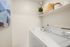 Bright laundry room featuring modern washer and dryer, elegant shelving with stylish decor, and soothing artwork on the wall.