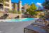 Inviting apartment complex featuring a sparkling pool surrounded by comfortable loungers and vibrant umbrellas, set against a backdrop of lush greenery and modern architecture.