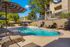 Inviting apartment complex pool area with sun loungers and vibrant umbrellas, perfect for relaxation under clear blue skies.