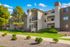 Charming apartment complex with modern architecture, surrounded by lush greenery and scenic pathways, under a brilliant blue sky.