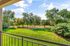 Expansive green community garden view from a serene apartment balcony, surrounded by lush trees under a bright blue sky.