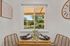 Charming dining nook with wicker chairs, a cozy wooden table set for two, and a picturesque window view of lush greenery.