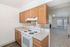 Bright and spacious kitchen with oak cabinetry and modern appliances opening into a sunlit living room with large windows and balcony view.