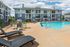 Inviting apartment complex with a sparkling blue swimming pool, modern lounge chairs, and beautifully maintained buildings under a bright blue sky.