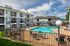 Charming apartment complex featuring a pristine pool, surrounded by modern buildings with private balconies and lush greenery.