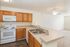 Bright and open kitchen with modern appliances, wooden cabinetry, and a spacious countertop overlooking a well-lit living area with ceiling fan.
