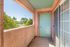 Charming apartment balcony with pastel peach walls and a refreshing mint green door, offering a serene view of lush greenery and a clear blue sky.