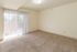 Bright and airy apartment room with plush carpet and large sliding glass doors, offering abundant natural light and serene views.