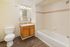 Elegant bathroom with modern lighting, sleek wooden cabinetry, a pristine white bathtub, and sophisticated tile accents.